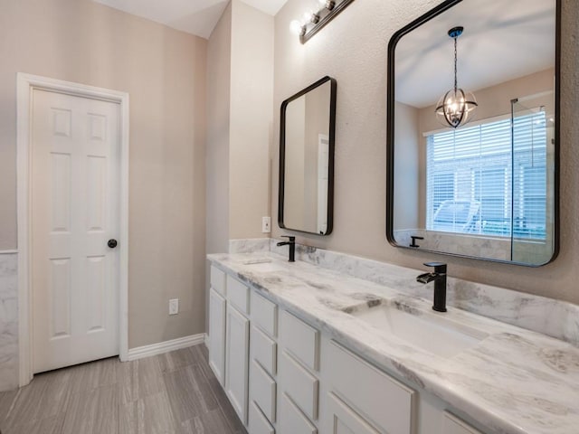 bathroom with baseboards, a sink, an inviting chandelier, and double vanity