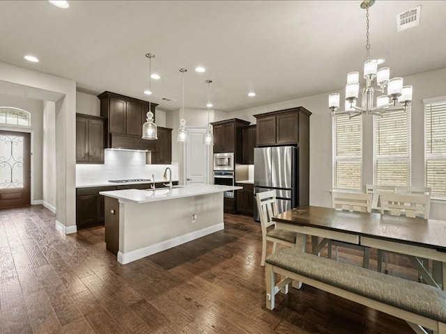 kitchen with a center island with sink, light countertops, visible vents, appliances with stainless steel finishes, and dark brown cabinets