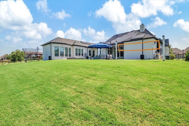 rear view of property featuring a chimney, fence, a yard, and roof mounted solar panels