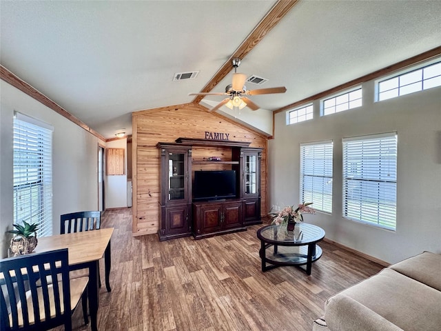 living area with ceiling fan, vaulted ceiling with beams, visible vents, wood walls, and wood finished floors