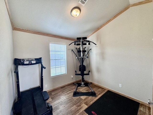 exercise room featuring wood finished floors, ornamental molding, baseboards, visible vents, and a textured ceiling