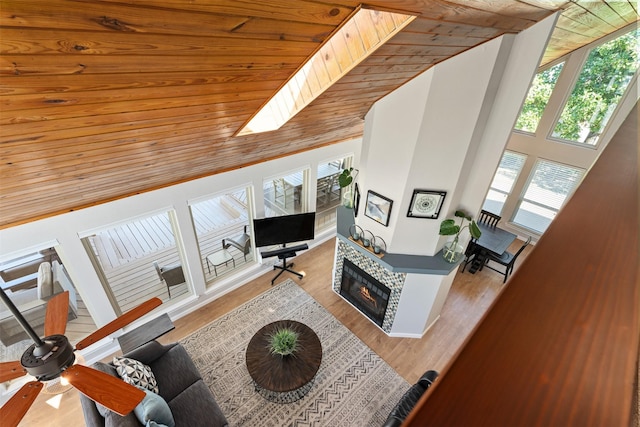 living room featuring a skylight, wood finished floors, a glass covered fireplace, and wooden ceiling