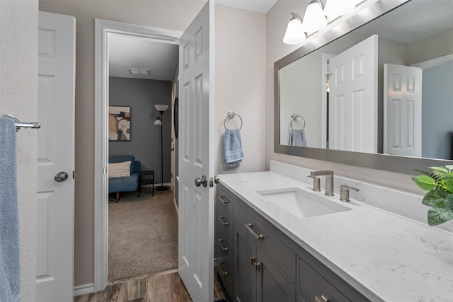 ensuite bathroom with visible vents, connected bathroom, baseboards, wood finished floors, and vanity