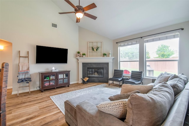 living room with arched walkways, visible vents, a tiled fireplace, light wood-style floors, and baseboards