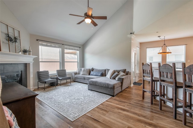 living room with ceiling fan, high vaulted ceiling, a fireplace, wood finished floors, and baseboards