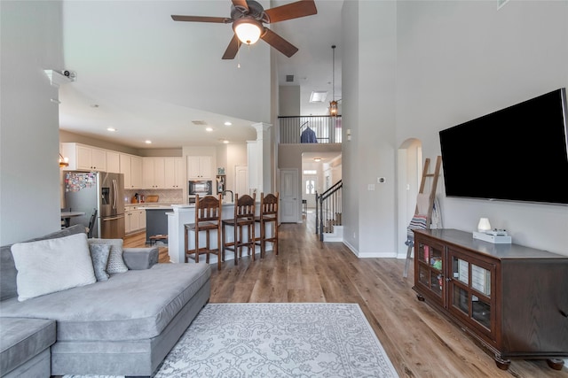 living area with baseboards, a ceiling fan, a towering ceiling, light wood-style flooring, and stairway