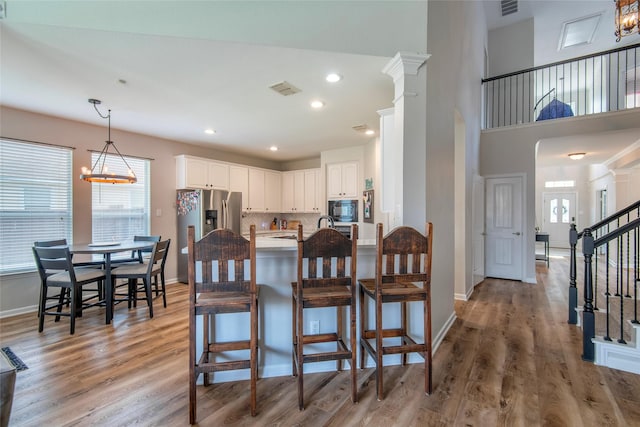 kitchen featuring black microwave, a peninsula, a kitchen breakfast bar, stainless steel refrigerator with ice dispenser, and light wood finished floors