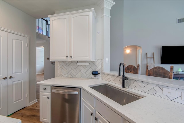 kitchen with tasteful backsplash, stainless steel dishwasher, white cabinets, a sink, and wood finished floors