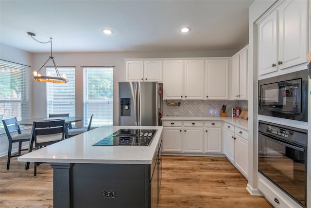 kitchen featuring white cabinetry, light wood-type flooring, backsplash, black appliances, and pendant lighting