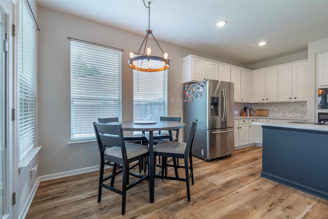 kitchen featuring black microwave, stainless steel fridge with ice dispenser, light wood-style floors, white cabinetry, and backsplash