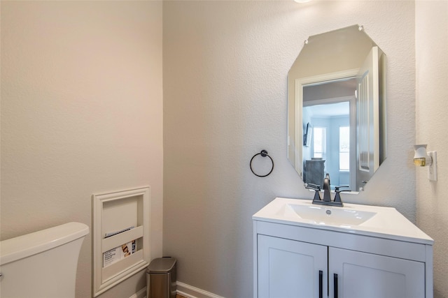 half bathroom featuring toilet, a textured wall, baseboards, and vanity