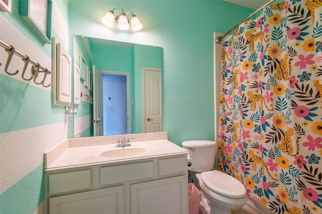 bathroom featuring a shower with shower curtain, a textured wall, vanity, and toilet