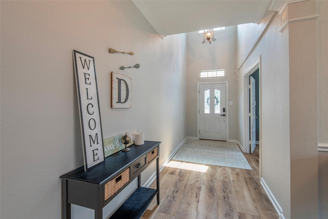 foyer with light wood-style floors, baseboards, ornamental molding, and a chandelier