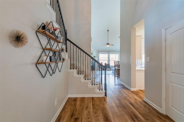 entryway with baseboards, a towering ceiling, ceiling fan, wood finished floors, and stairs