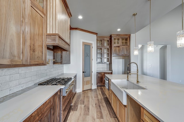 kitchen with light wood-style flooring, a sink, light countertops, glass insert cabinets, and stainless steel gas stovetop