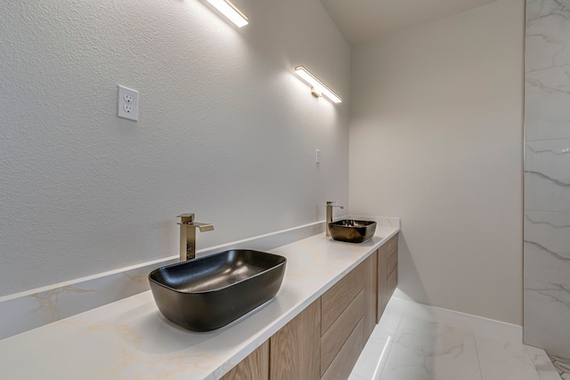 bathroom featuring double vanity, marble finish floor, baseboards, and a sink