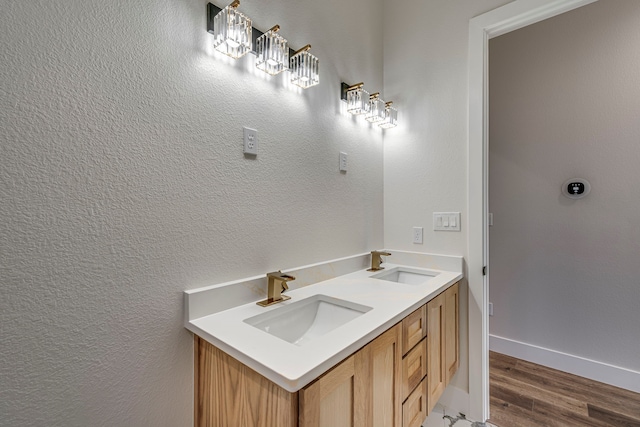 bathroom with a textured wall, wood finished floors, a sink, and baseboards