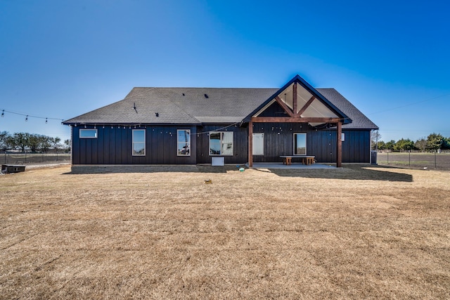 back of property featuring board and batten siding, a lawn, fence, and roof with shingles