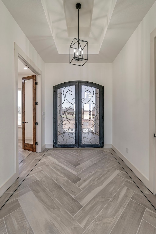 entrance foyer with a raised ceiling, baseboards, french doors, and an inviting chandelier