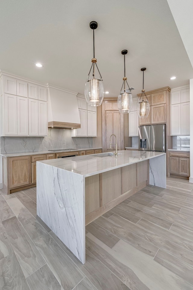 kitchen featuring electric cooktop, a spacious island, a sink, custom exhaust hood, and stainless steel fridge with ice dispenser