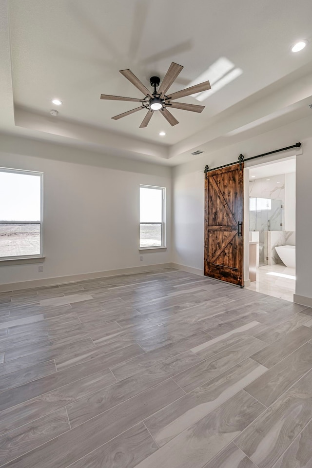 empty room with a barn door, a tray ceiling, baseboards, and recessed lighting