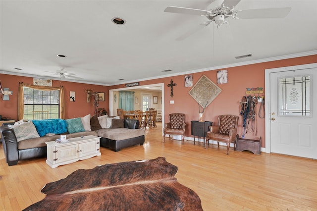 living room with a ceiling fan, visible vents, baseboards, ornamental molding, and light wood finished floors