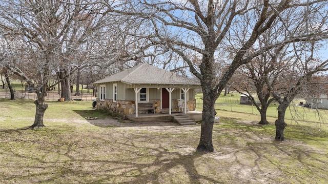 view of front of property featuring a porch, fence, stone siding, roof with shingles, and a front yard