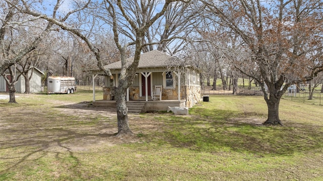 exterior space featuring stone siding, an outbuilding, roof with shingles, covered porch, and a front lawn