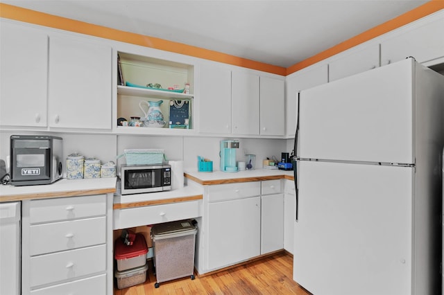 kitchen with white cabinets, light wood-style flooring, stainless steel microwave, freestanding refrigerator, and light countertops