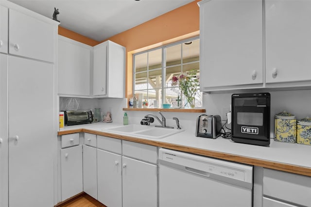 kitchen with white cabinets, light countertops, dishwasher, and a sink