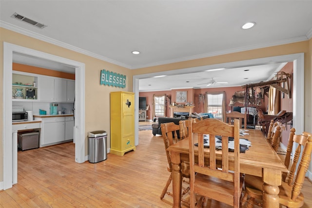 dining area featuring ornamental molding, visible vents, a fireplace, and light wood finished floors