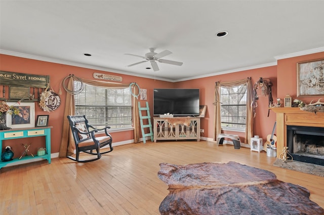 living room with hardwood / wood-style flooring, a fireplace, a ceiling fan, baseboards, and ornamental molding