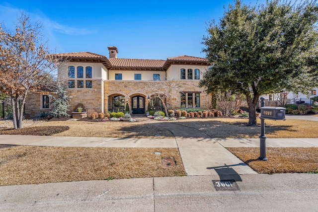 mediterranean / spanish house featuring stone siding, a chimney, a tiled roof, and stucco siding