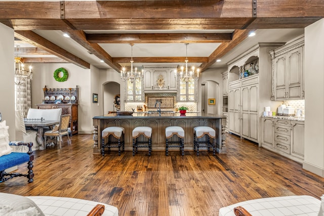 kitchen featuring arched walkways, dark wood-type flooring, a breakfast bar area, and tasteful backsplash