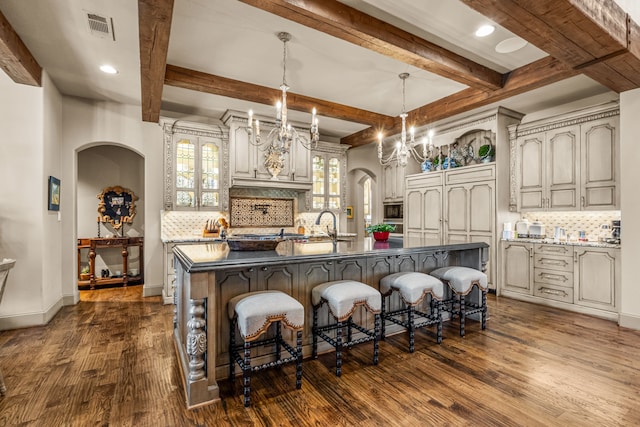 kitchen featuring visible vents, arched walkways, a breakfast bar area, dark wood-type flooring, and a large island with sink