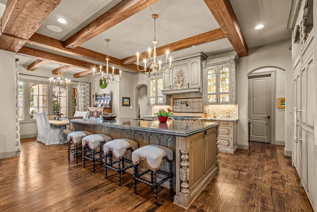 kitchen with arched walkways, decorative backsplash, dark wood-type flooring, a large island with sink, and a kitchen bar