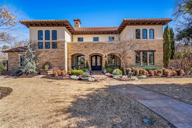 mediterranean / spanish-style house featuring stone siding, a tile roof, a chimney, french doors, and stucco siding