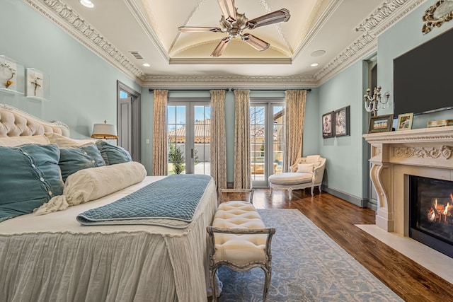 bedroom featuring a fireplace with flush hearth, wood finished floors, access to outside, a tray ceiling, and crown molding