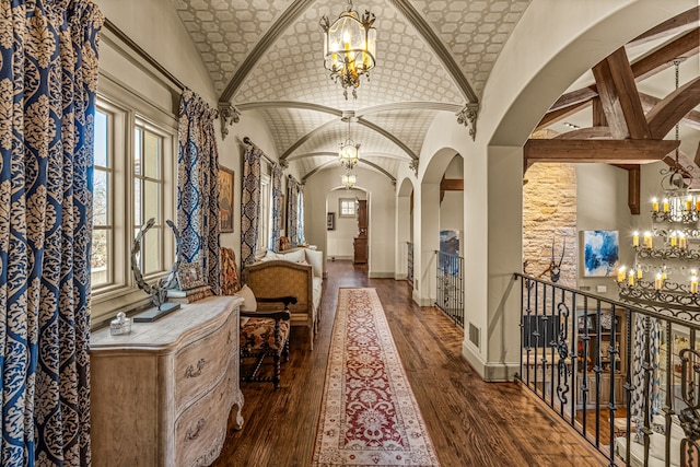 hall featuring arched walkways, a notable chandelier, wood-type flooring, vaulted ceiling, and baseboards