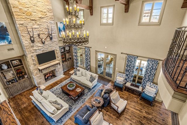 living room featuring a notable chandelier, a stone fireplace, wood finished floors, and french doors