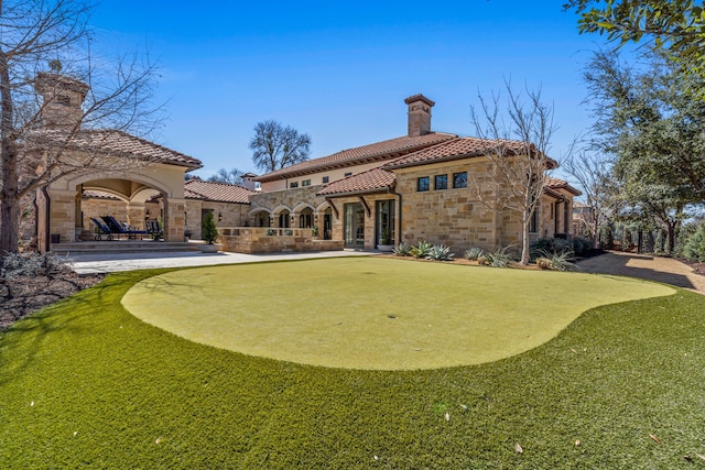 rear view of property featuring a patio area, stone siding, a tile roof, and a chimney