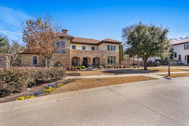 mediterranean / spanish house with stone siding, a tile roof, a chimney, and stucco siding