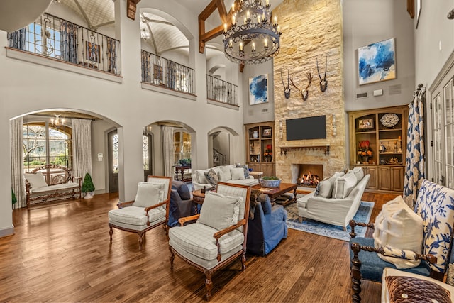 interior space with an inviting chandelier, arched walkways, wood finished floors, and a stone fireplace