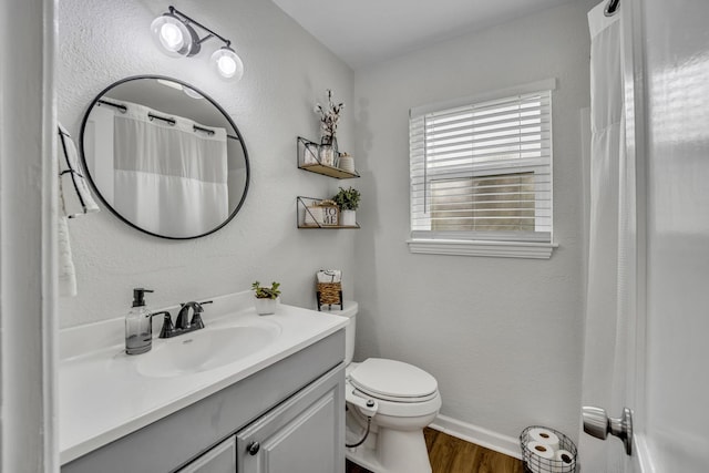 full bath featuring a textured wall, toilet, vanity, wood finished floors, and baseboards