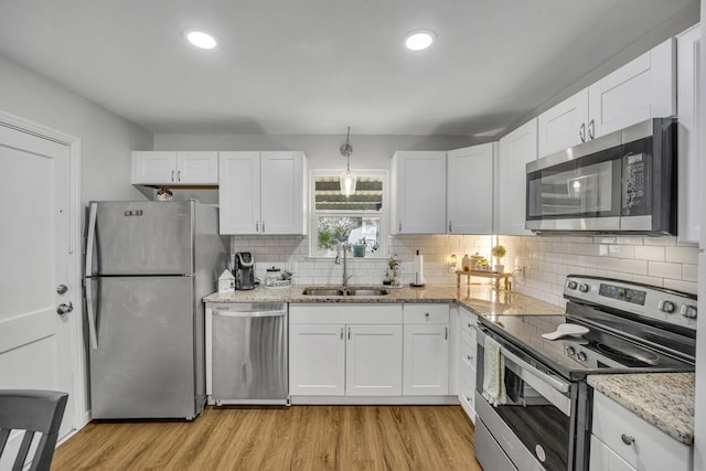 kitchen with a sink, white cabinets, light wood-style floors, appliances with stainless steel finishes, and light stone countertops