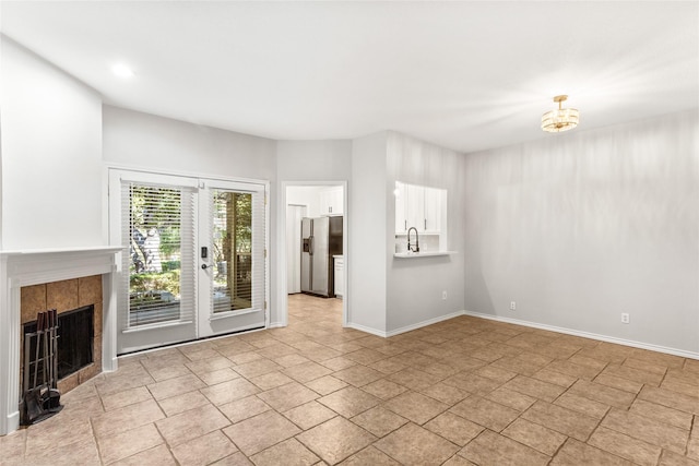 unfurnished living room featuring baseboards, french doors, a sink, and a tile fireplace