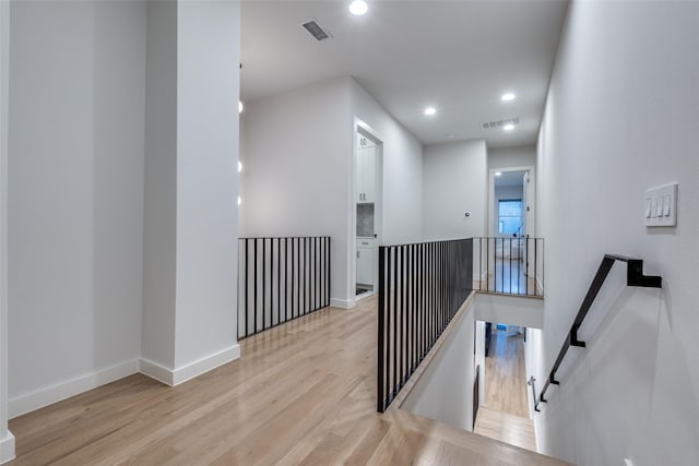 hallway with baseboards, visible vents, wood finished floors, an upstairs landing, and recessed lighting