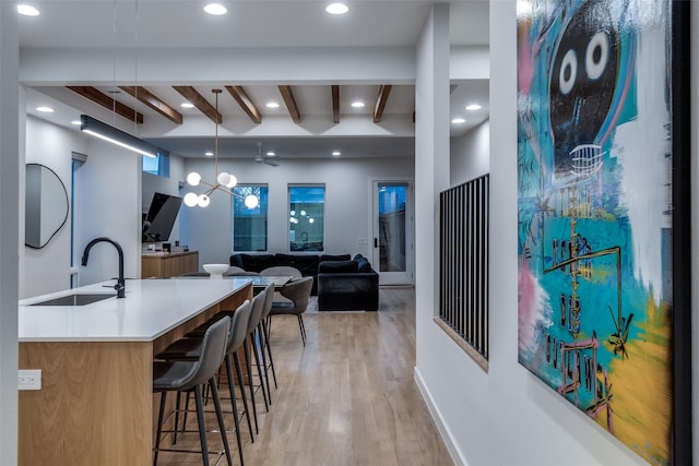 kitchen featuring light wood finished floors, hanging light fixtures, a sink, beam ceiling, and recessed lighting