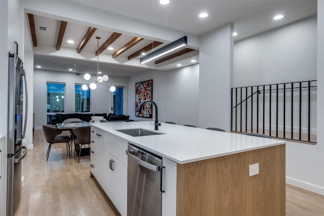 kitchen featuring light wood finished floors, white cabinets, open floor plan, stainless steel appliances, and a sink