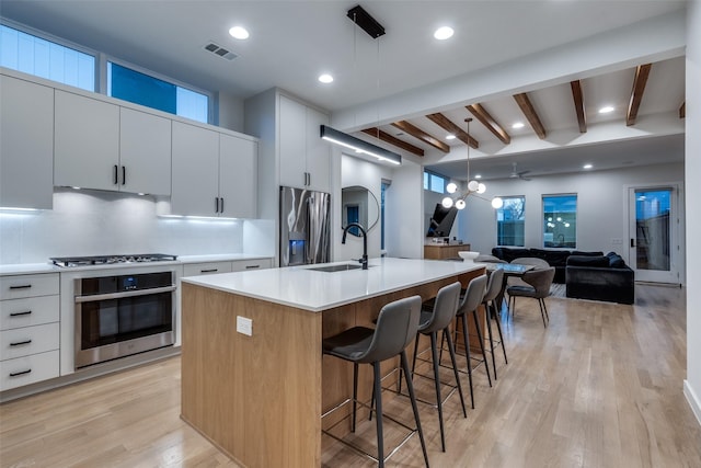 kitchen featuring stainless steel appliances, a sink, light countertops, light wood-type flooring, and backsplash